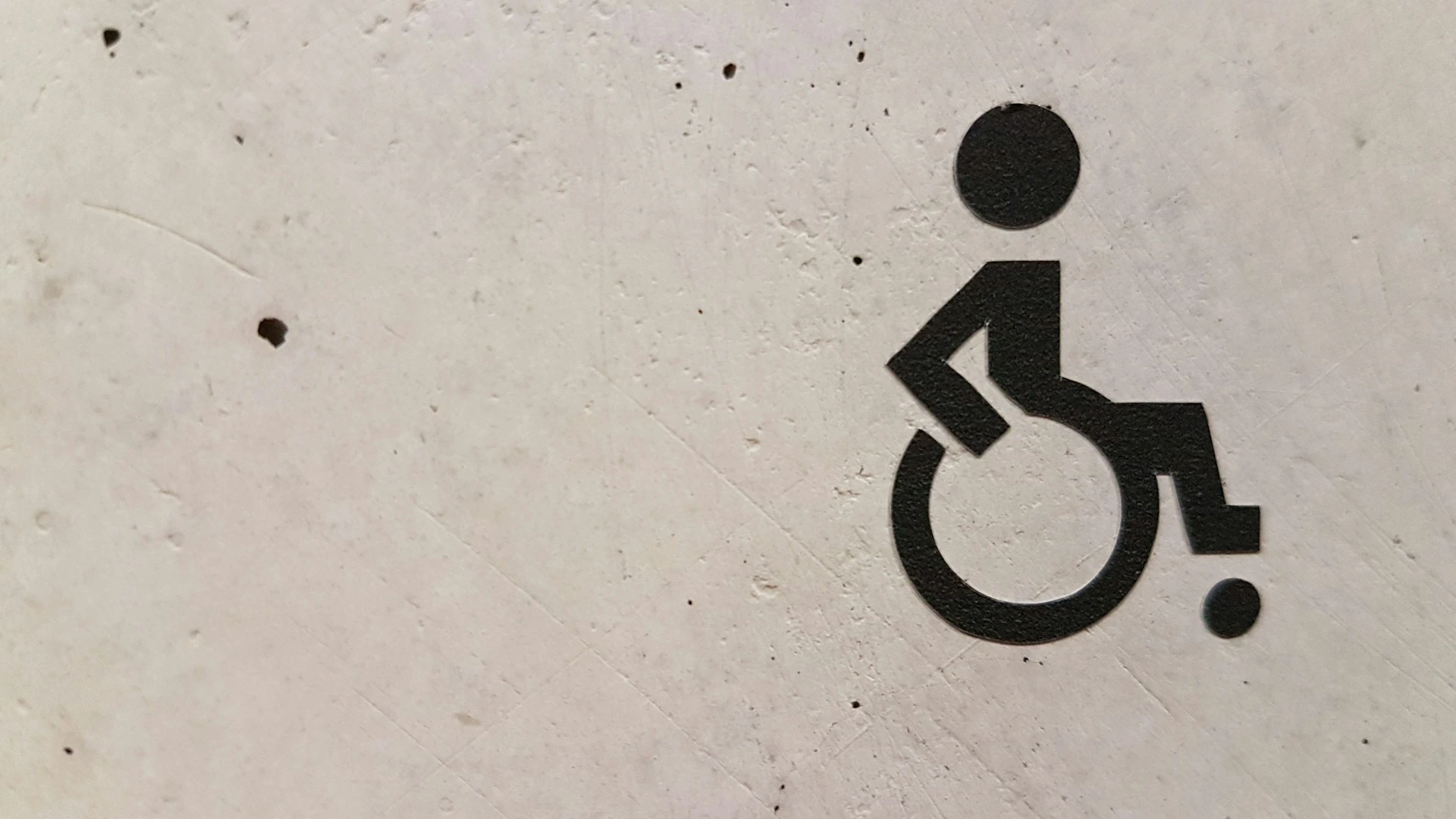 The image shows a black icon of a disabled person in a wheelchair on a concrete background.